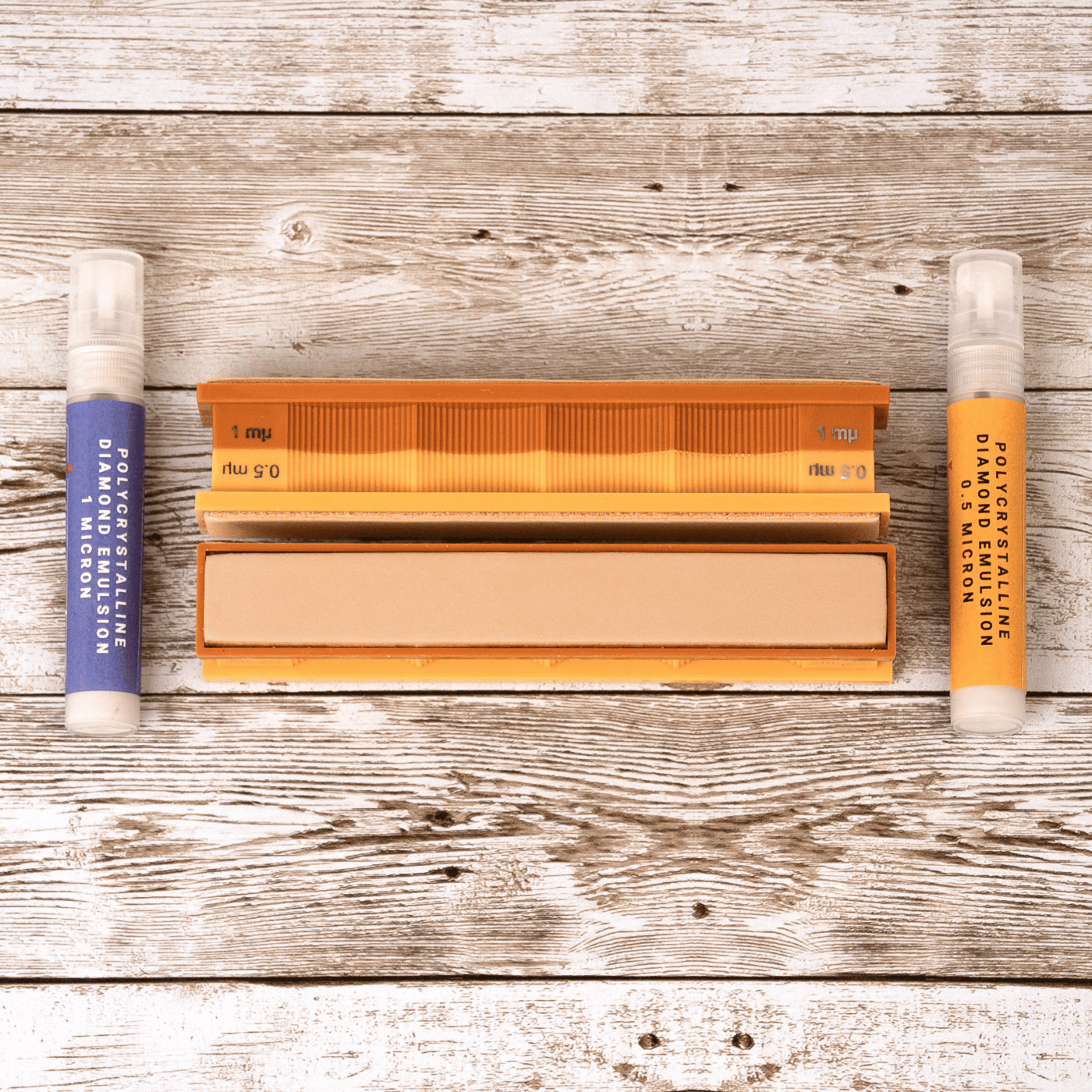 1/0.5 Micron Diamond Emulsion and Leather Strops Pack in close-up view on weathered wood surface.
