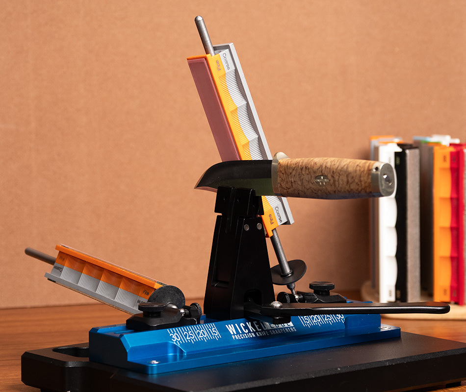 Blank glass platen handles and orange fine/grey coarse lapping film inserts on Wicked Edge precision knife sharpener base at close-up zoom from front angle.