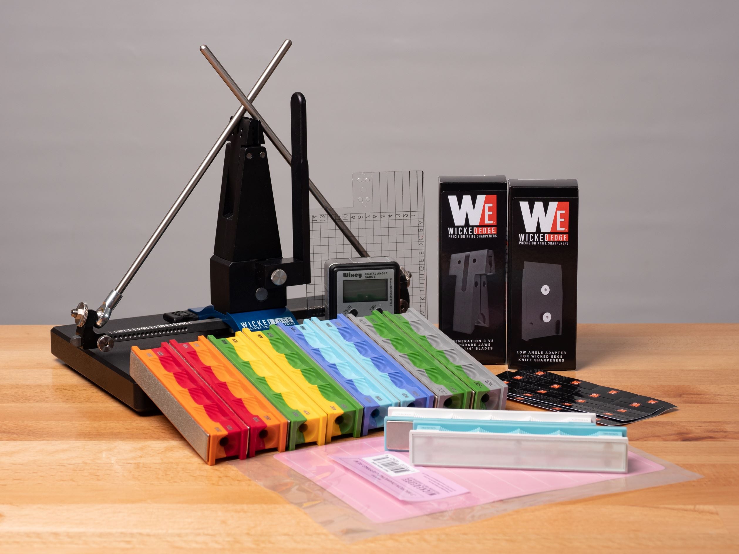Pro-Pack III knife sharpening kit with colored angle guide rods, digital angle cube, and assorted diamond stones on wooden table, close-up front view.