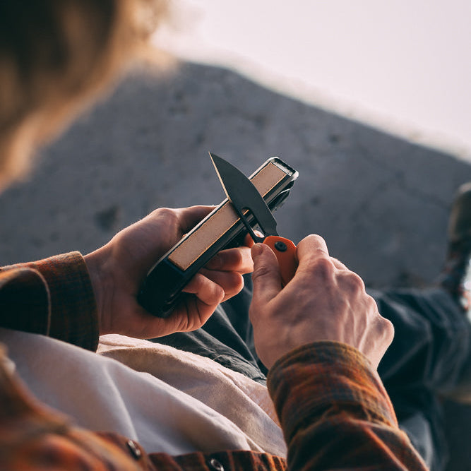 A close-up lifestyle shot of a person outdoors, using the leather strop on the Venture knife sharpener
