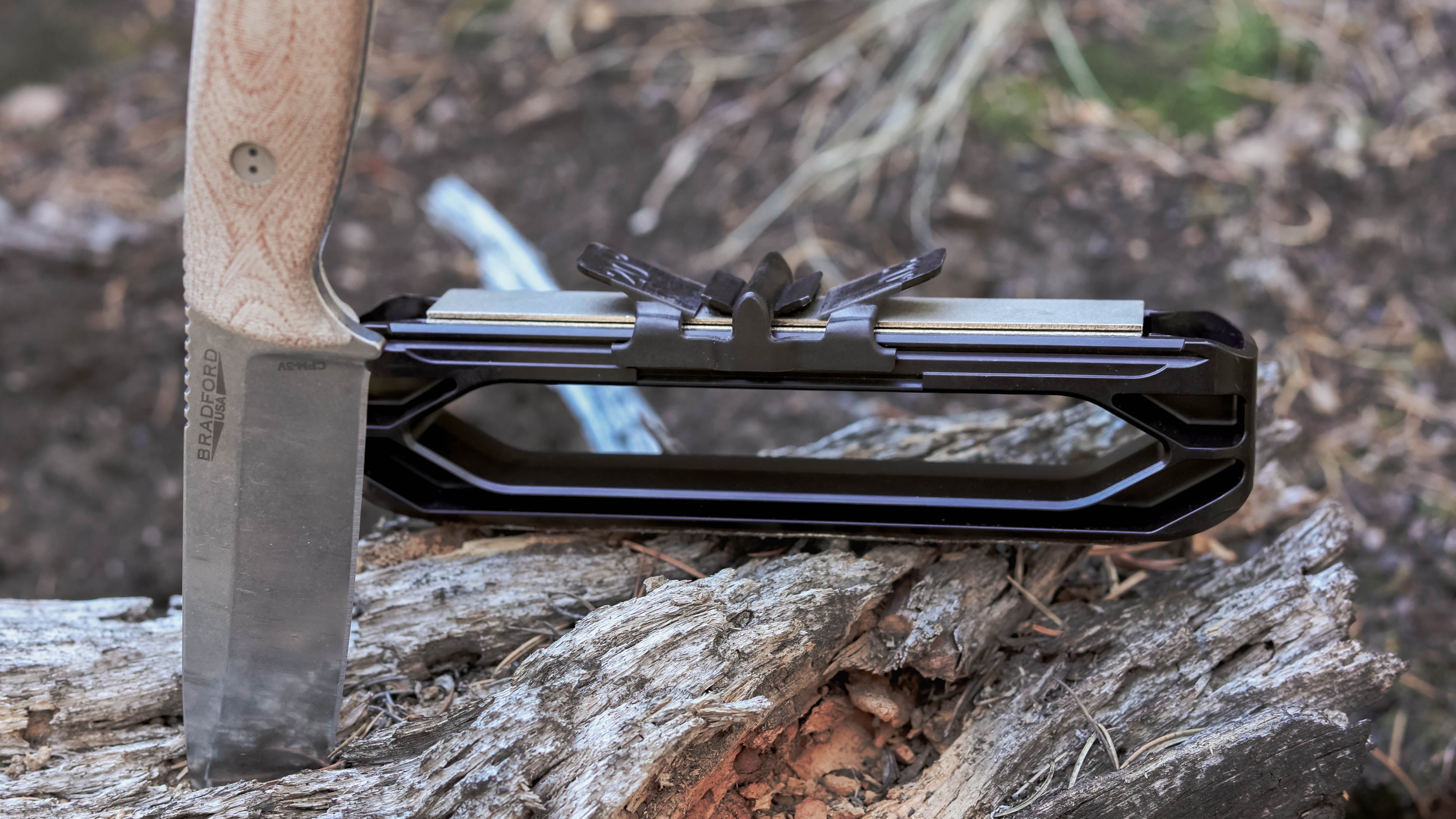 a Venture Knife Sharpener sitting on a log sitting next to a knife stabbed into the same log. 