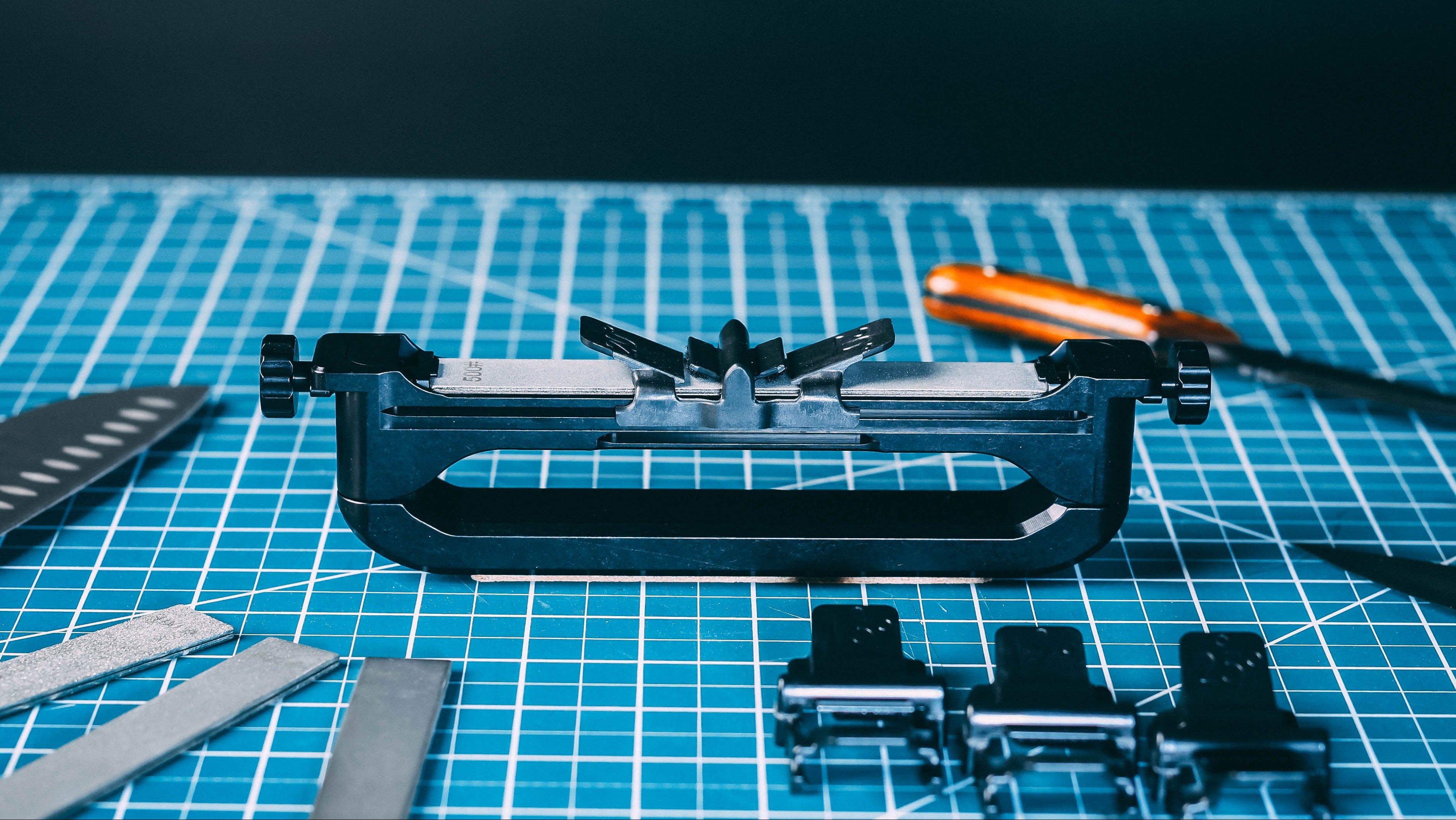 Wicked Edge Venture Pro set up on a blue mat. Various accessories and knifes are scattered around the Venture Pro