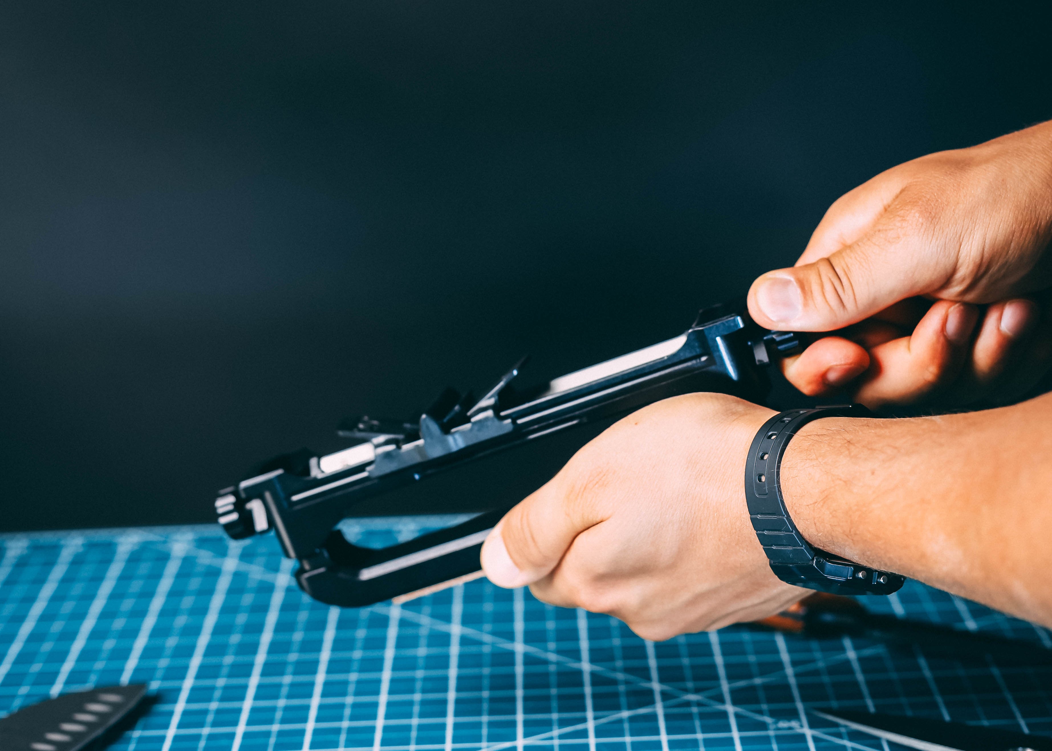 A close-up of a person's hands holding and WE26 Venture Pro, over a blue gridded cutting mat with small metal parts scattered around.