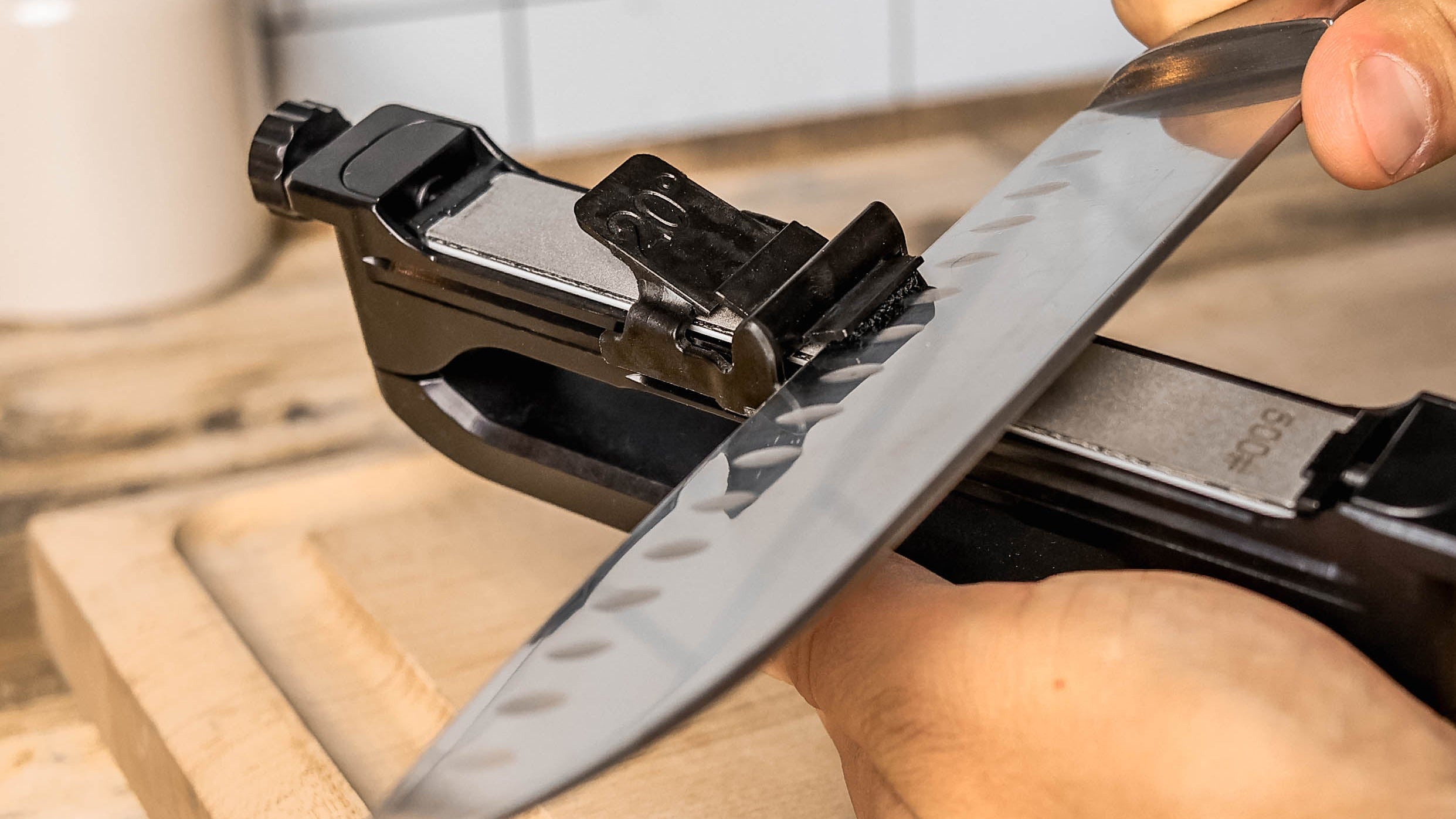 A close-up of a person sharpening a kitchen knife using a Venture Pro on a wooden cutting board in a kitchen setting.